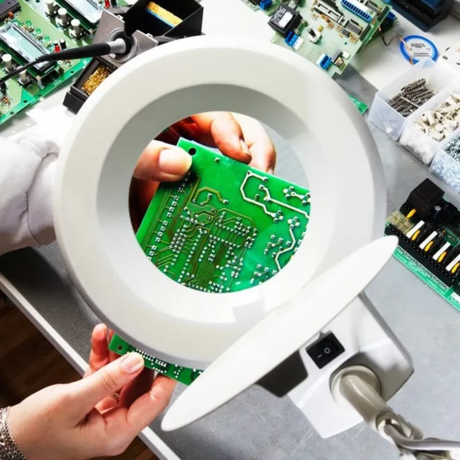 A close-up of a worker inspecting a PCB using testing equipment.